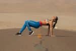 woman in red sports bra and blue leggings doing yoga on gray sand during daytime