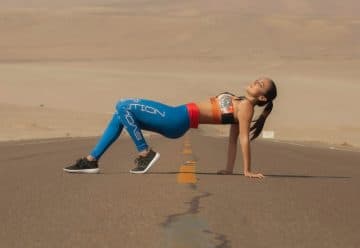 woman in red sports bra and blue leggings doing yoga on gray sand during daytime